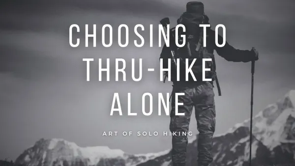 Black and white photo of a hiker on the top of a peak looking out over other mountains